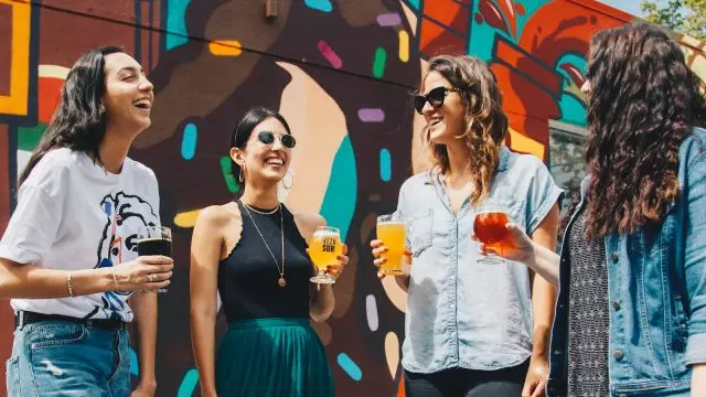 four women holding drinks while laughing together during daytime